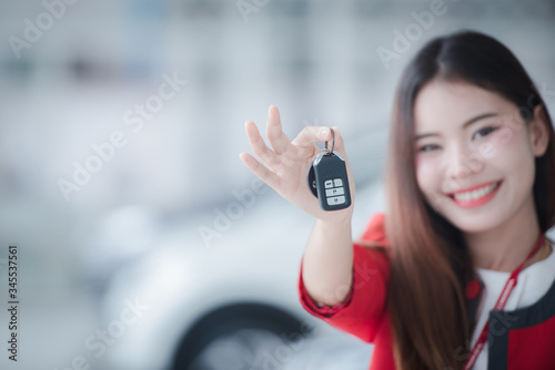 Asian car driver woman smiling showing new car keys and car. Mixed-race Asian and Caucasian girl.