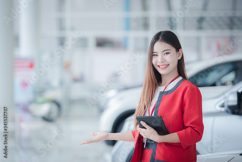 A beautiful Asian car saleswoman is happy to sell a new car in the showroom and enjoy selling the car.