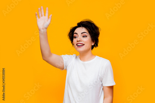 Young happy brunette woman with a short haircut in a white T-shirt on a yellow background. portrait of a young woman with various emotions on a yellow background. space for text