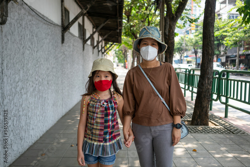 Portrait photo of Asian mother and her daughter wearing medical face mask while walking in the city.