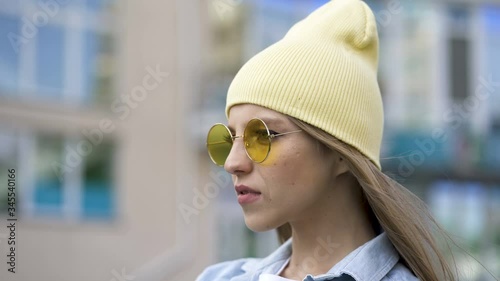 4k. Young girl in yellow cap and glasses stand in  city area. Street portrait