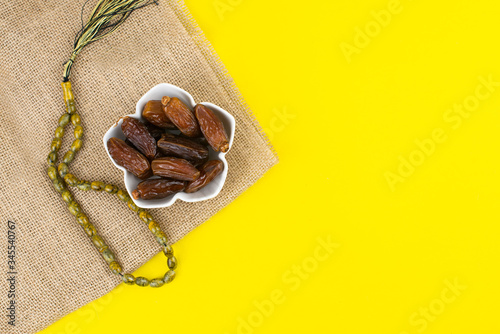 Ramadan Kareem Festival. Close up of dried dates fruit in bowl with rosary on yellow background. Copy space.