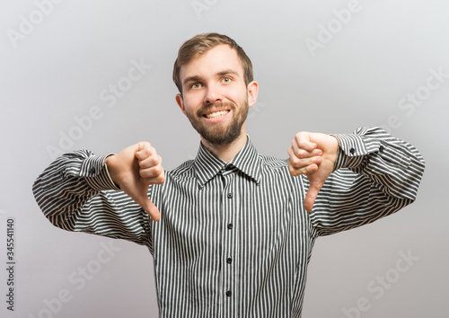 Foto Closeup portrait of sarcastic young man showing two thumbs down sign hand gesture, happy that someone made mistake, lost, failed isolated white background