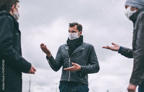 young people in protective masks talk standing at a safe distance