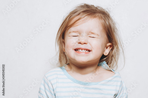 portrait of a little girl of 2 years wearing a red hat and being photographed showing different emotions against a light wall