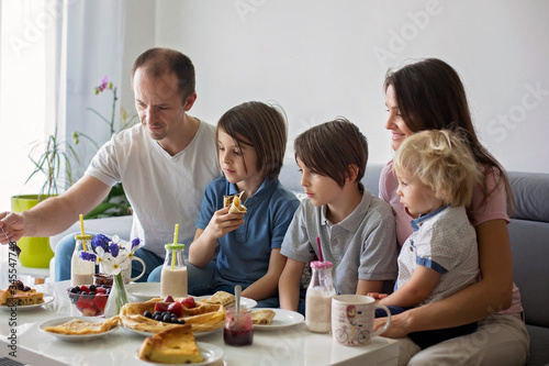 Happy family, having pancakes for breakfast, eating in living room, talking and lauging