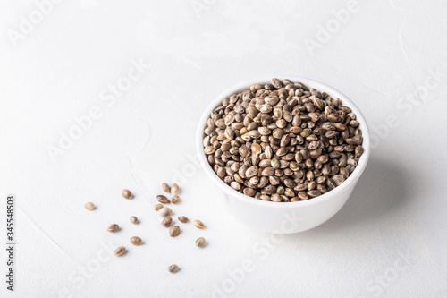 Raw organic unrefined hemp seeds in small white bowl on white concrete background.