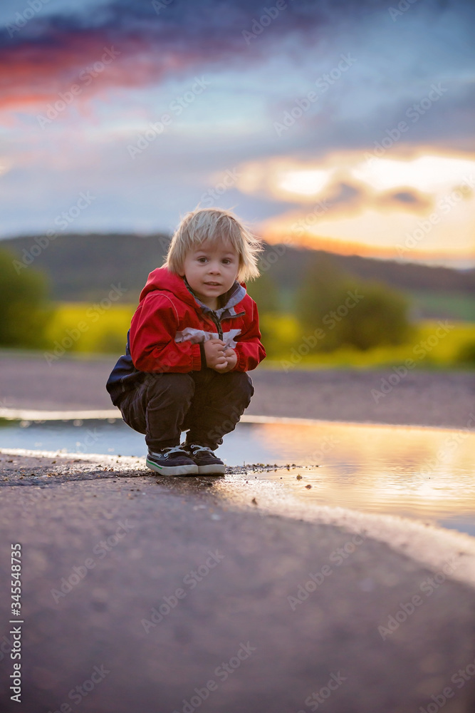 Sweet toddler child, cute boy with red raincoat, playing in puddle Sweet toddler child, cute boy with red raincoat, playing in puddle