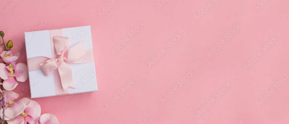 A gift box and pink orchids on a pink background. Gift box background.