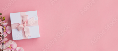 A gift box and pink orchids on a pink background. Gift box background.