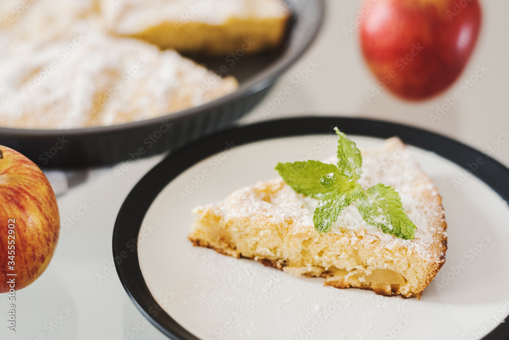 Piece of apple pie served with icing sugar and fresh mint leaves. Sponge cake