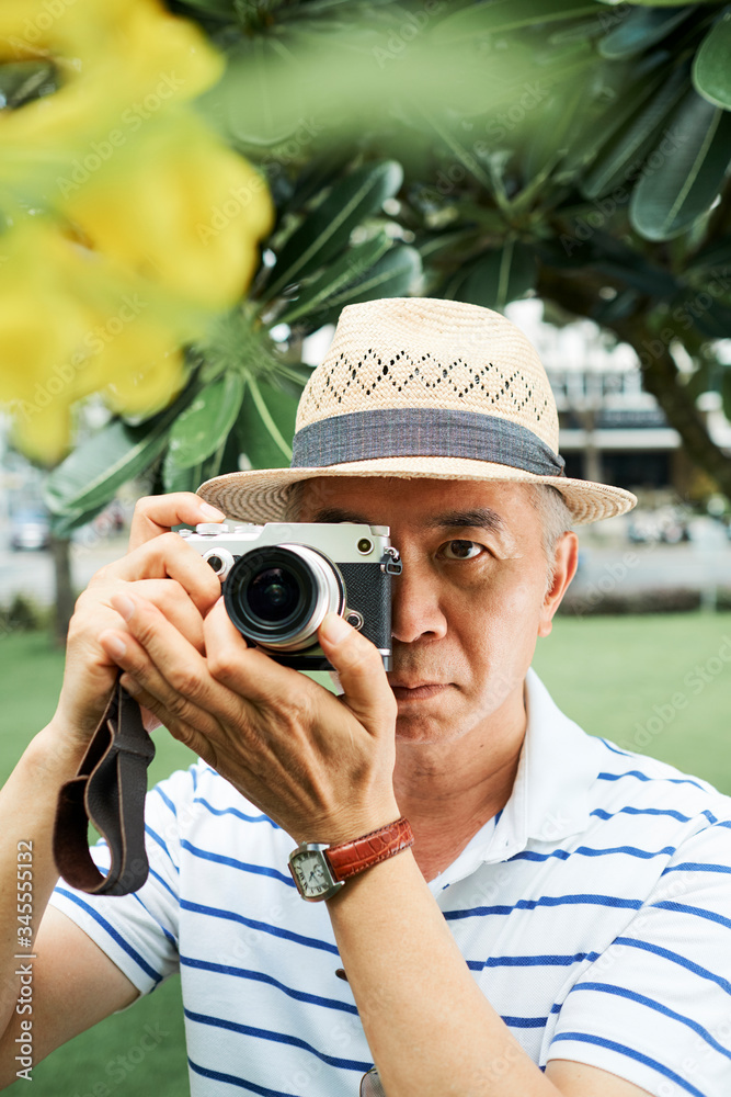 Concentrated senior Chinese man trying to make a perfect photo of blooming tree Concentrated senior Chinese man trying to make a perfect photo of blooming tree