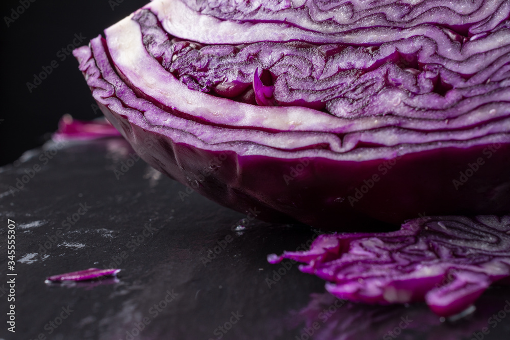 Close-up of red cabbage with pieces, selective focus, on wet black slate, black background, horizontal