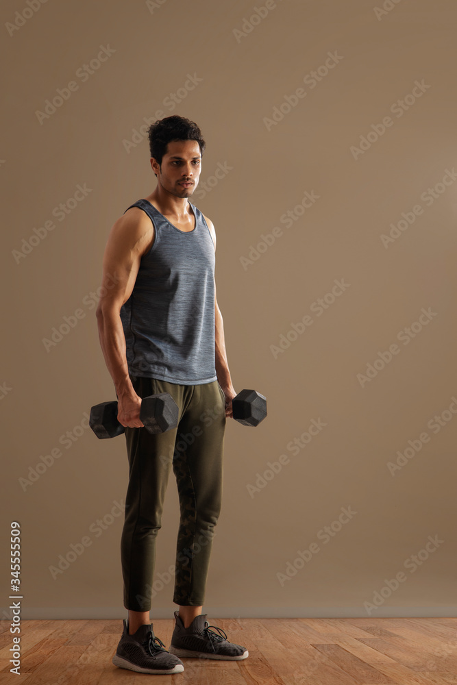 Man standing with dumbbells in his hand in front of a plain background.
Man standing with dumbbells in his hand in front of a plain background.