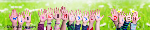Children Hands Building Colorful German Word Wir Vermissen Dich Means We Miss You. Sunny Green Grass Meadow As Background