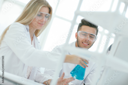 smiling scientist showing his colleague a flask of liquid.