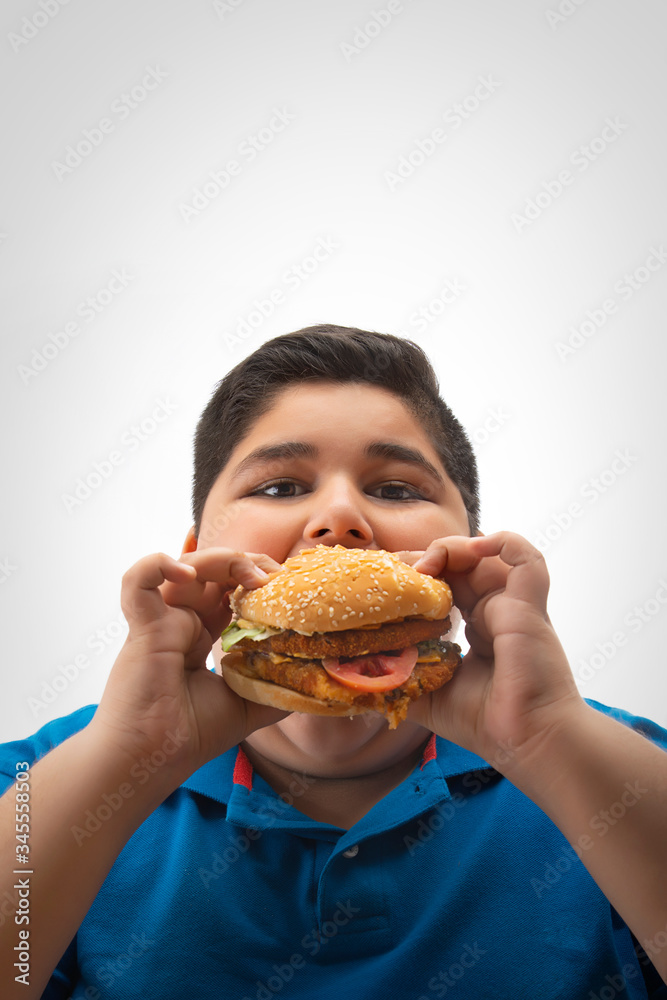 Young boy eating a large burger in hand. (Obesity) Young boy eating a large burger in hand. (Obesity)