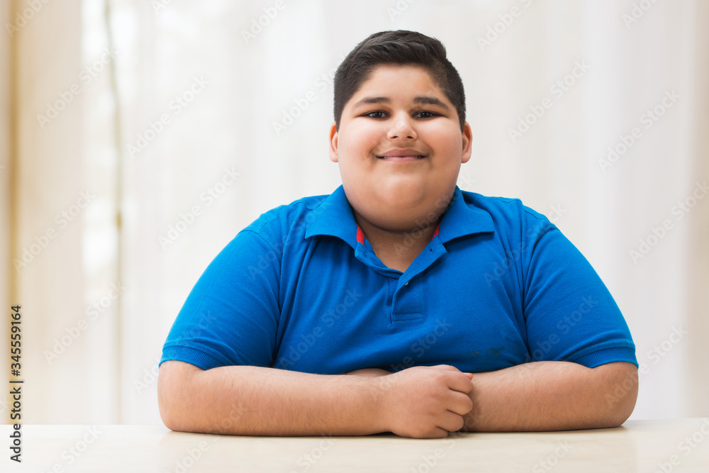 Portrait of a chubby boy sitting with his hands on the table. (Obesity) Portrait of a chubby boy sitting with his hands on the table. (Obesity)