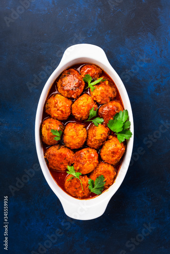 Meatballs with tomato sauce and spices in baking dish on blue kitchen table background. Top View with copy space