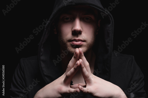 A man in a black hood on a black background, studio photography. The idea of mysticism, mystery, crime and deception