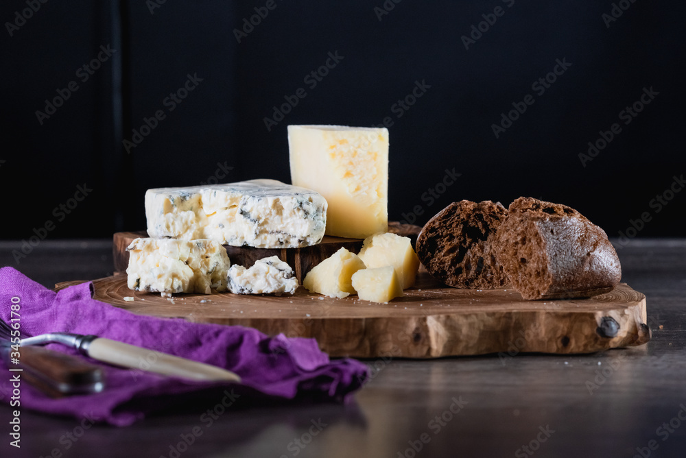 Cheese and bread on a wooden stand on the table dark background. The concept of nutrition and beautiful serving of food.