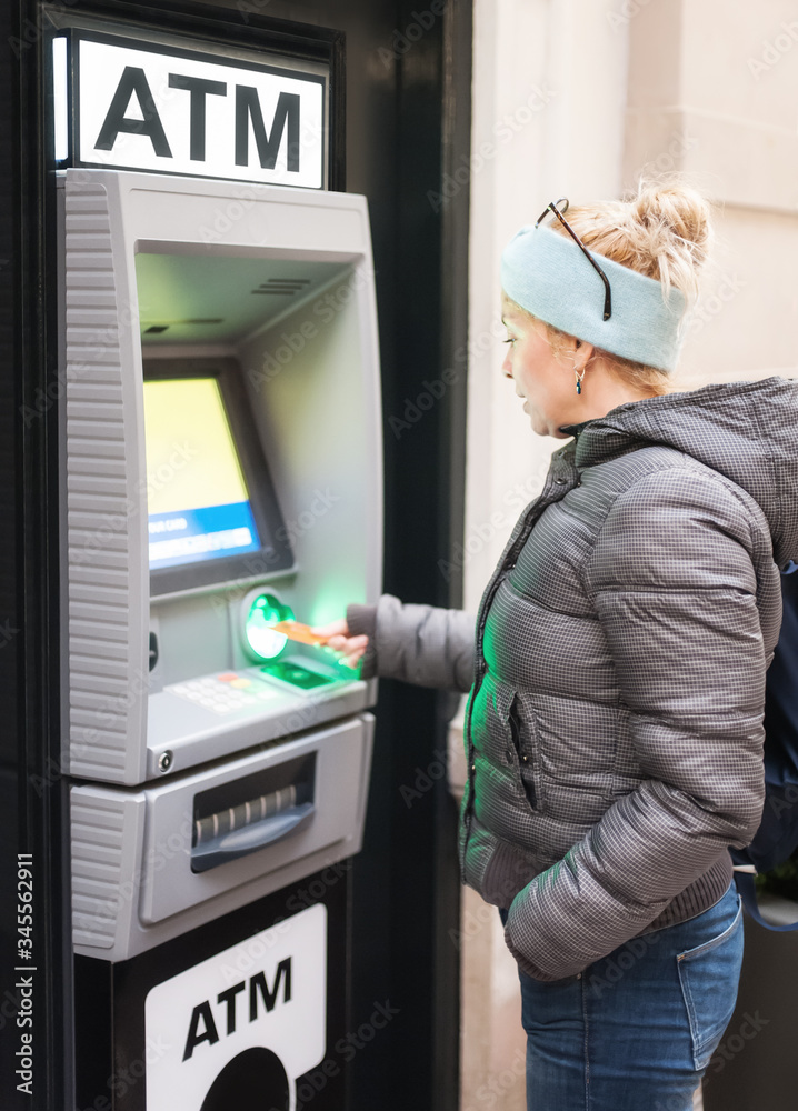 Side view of an female withdrawing the money from a bank card using street ATM machine, inserting her bank card into an automated teller machine Side view of an female withdrawing the money from a bank card using street ATM machine, inserting her bank card into an automated teller machine