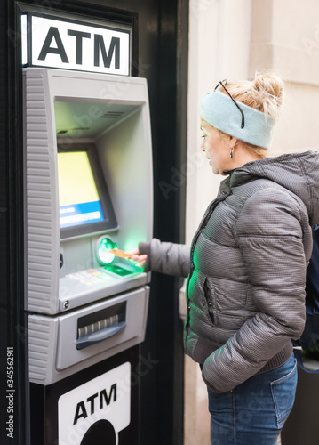 Side view of an female withdrawing the money from a bank card using street ATM machine, inserting her bank card into an automated teller machine