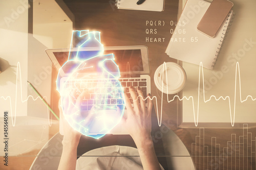 Double exposure of woman hands working on computer and heart hologram drawing. Top View. Medical Science concept.