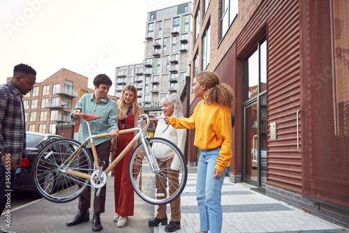 Group Of Multi-Cultural Friends On City Street Lifting Sustainable Bamboo Bicycle 