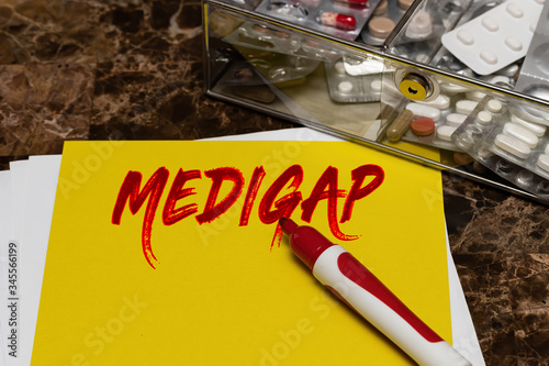 Medigap is written in red letters on a yellow sheet lying on the table next to a box of pills. photo