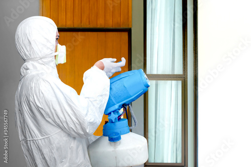 Man in a white protective suit spraying disinfectant on the home