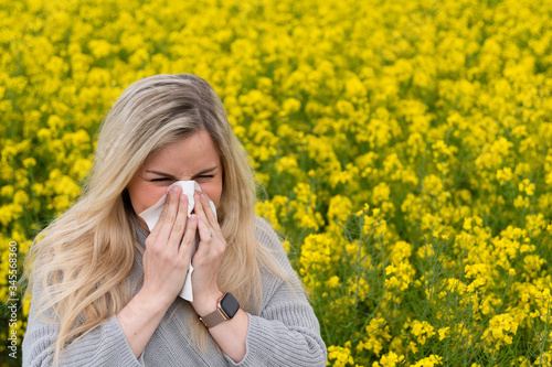 Tablou pe pânză Young woman suffers from allergy in a rape field and has to sneeze