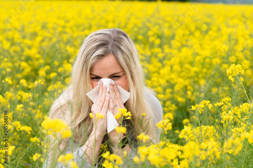Young woman suffers from allergy in a rape field and has to sneeze