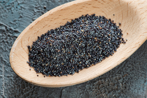 in a light wooden spoon, a pile of poppy seeds seen very closely