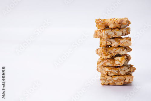 Jaggery in a wooden spoon with plain peanuts kept with chikki and groundnuts on a white tray
 photo