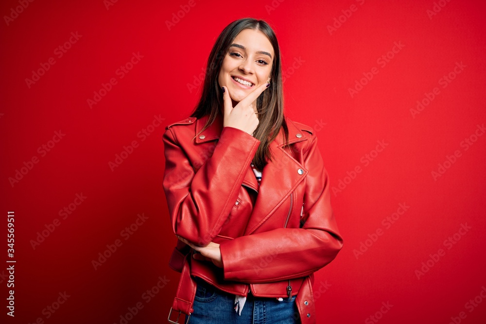 Young beautiful brunette woman wearing casual jacket standing over red background looking confident at the camera smiling with crossed arms and hand raised on chin. Thinking positive. Young beautiful brunette woman wearing casual jacket standing over red background looking confident at the camera smiling with crossed arms and hand raised on chin. Thinking positive.