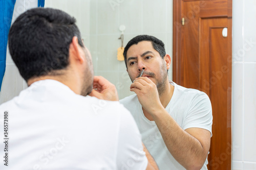 Man cutting his nose hairs with a small scissor in front of the mirror in his home bathroom