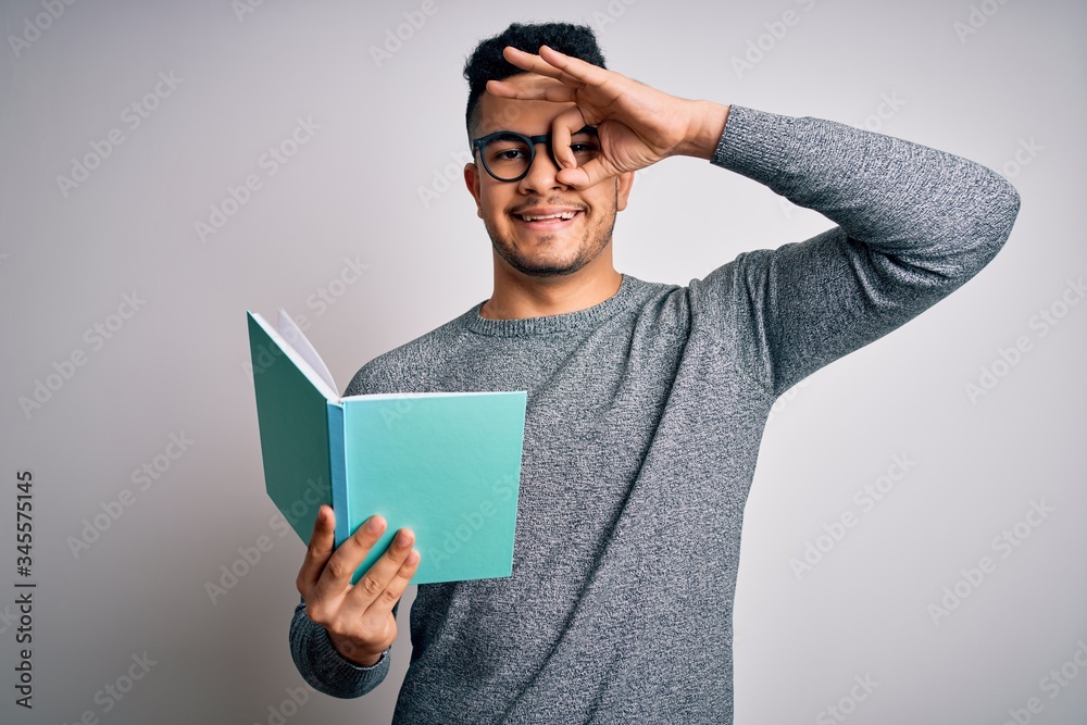 Young handsome smart student man reading book over isolated white background with happy face smiling doing ok sign with hand on eye looking through fingers Young handsome smart student man reading book over isolated white background with happy face smiling doing ok sign with hand on eye looking through fingers