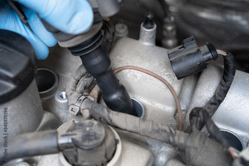 Man in protective glove removing ignition coil in car engine bay. Mechanic repair or vehicle maintenance concept.