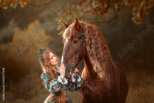 Beautiful long-haired blonde young woman in national russian style with red Vladimir draft horse in autumn forest © Julia Shepeleva