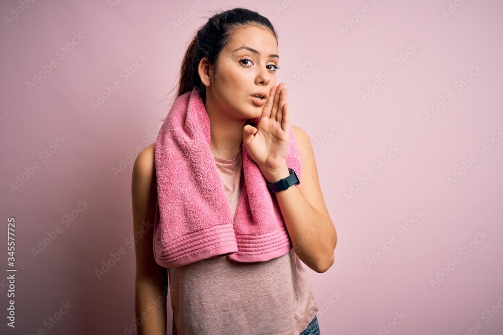 Young beautiful brunette sportswoman wearing sportswear and towel over pink background hand on mouth telling secret rumor, whispering malicious talk conversation Young beautiful brunette sportswoman wearing sportswear and towel over pink background hand on mouth telling secret rumor, whispering malicious talk conversation