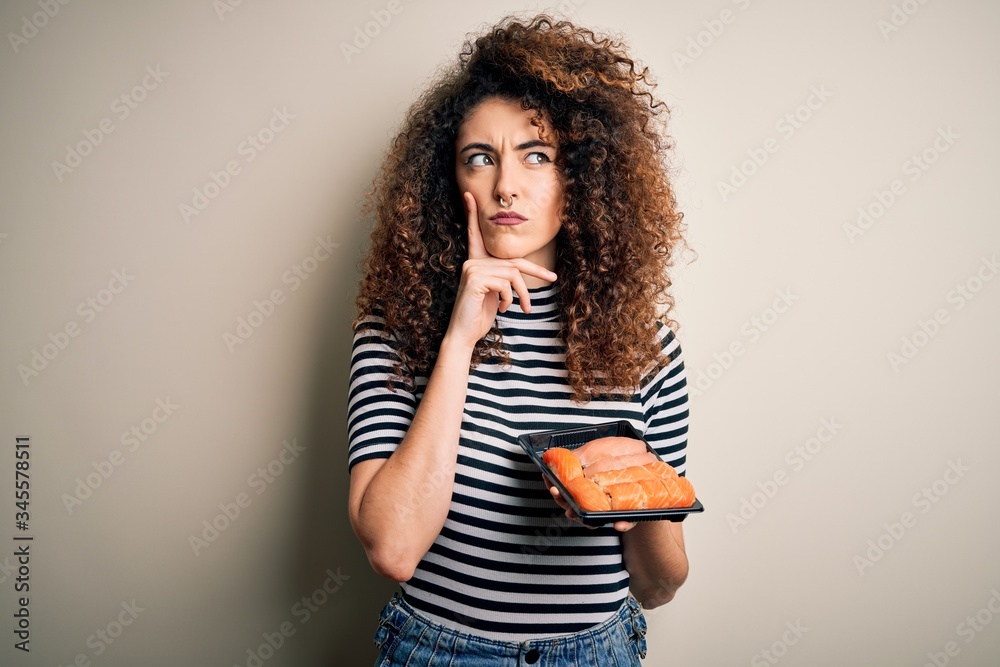Young beautiful woman with curly hair and piercing holding tray with fresh sushi serious face thinking about question, very confused idea Young beautiful woman with curly hair and piercing holding tray with fresh sushi serious face thinking about question, very confused idea