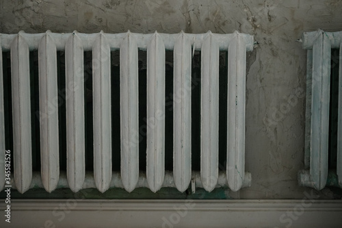 Old white iron radiator central heating on brick wall in room. It's cold in the house.