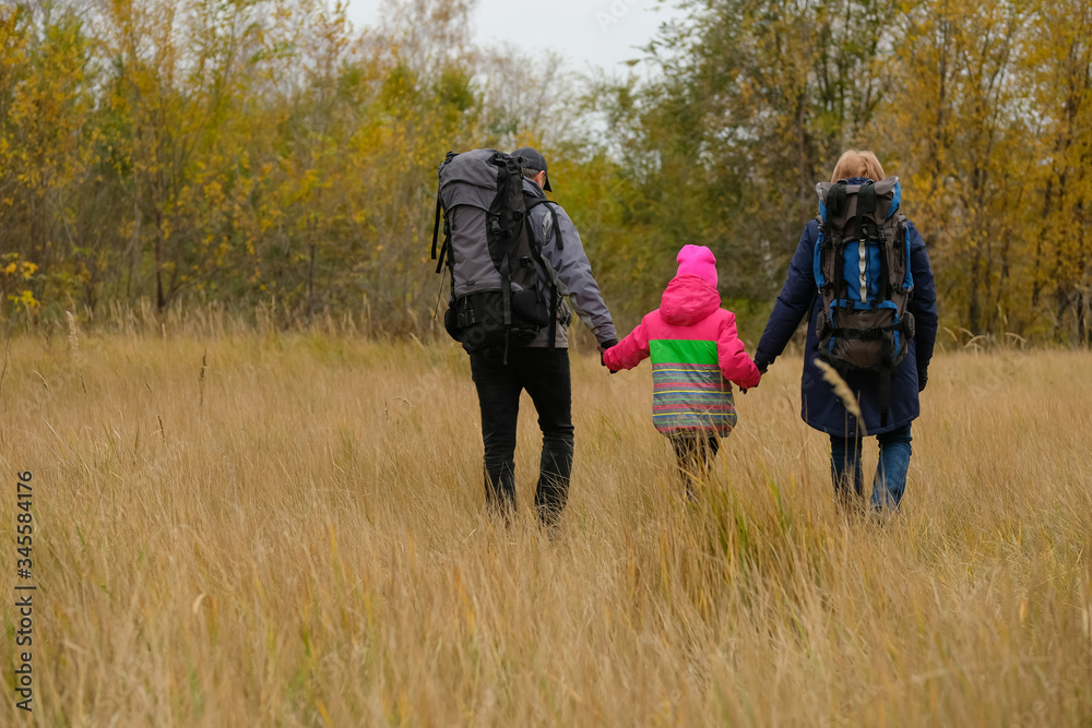 Mom, dad and daughter go camping. Family of tourists with backpacks on the background of autumn forest. Mom, dad and daughter go camping. Family of tourists with backpacks on the background of autumn forest.