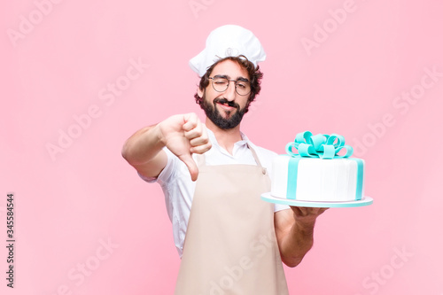 young crazy baker man holding a cake against pink wall