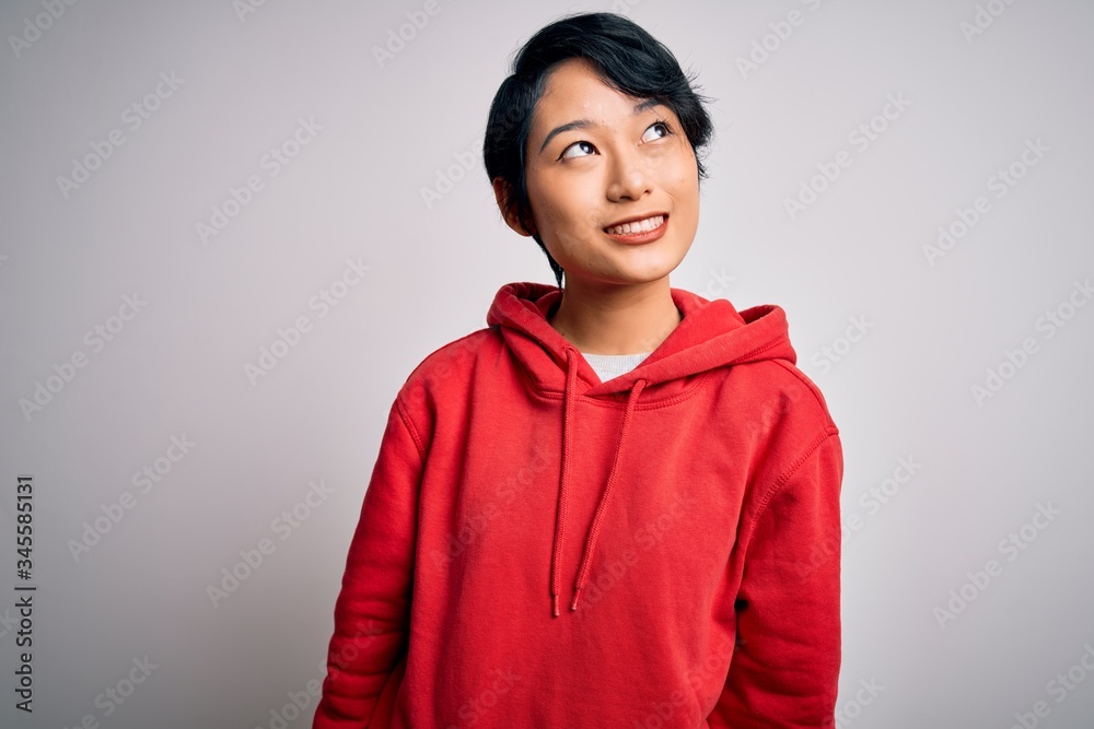 Young beautiful asian girl wearing casual sweatshirt with hoodie over white background looking away to side with smile on face, natural expression. Laughing confident. Young beautiful asian girl wearing casual sweatshirt with hoodie over white background looking away to side with smile on face, natural expression. Laughing confident.