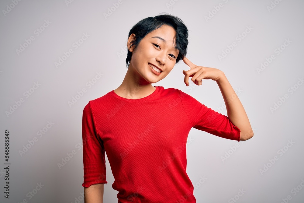 Young beautiful asian girl wearing casual red t-shirt standing over isolated white background Smiling pointing to head with one finger, great idea or thought, good memory Young beautiful asian girl wearing casual red t-shirt standing over isolated white background Smiling pointing to head with one finger, great idea or thought, good memory