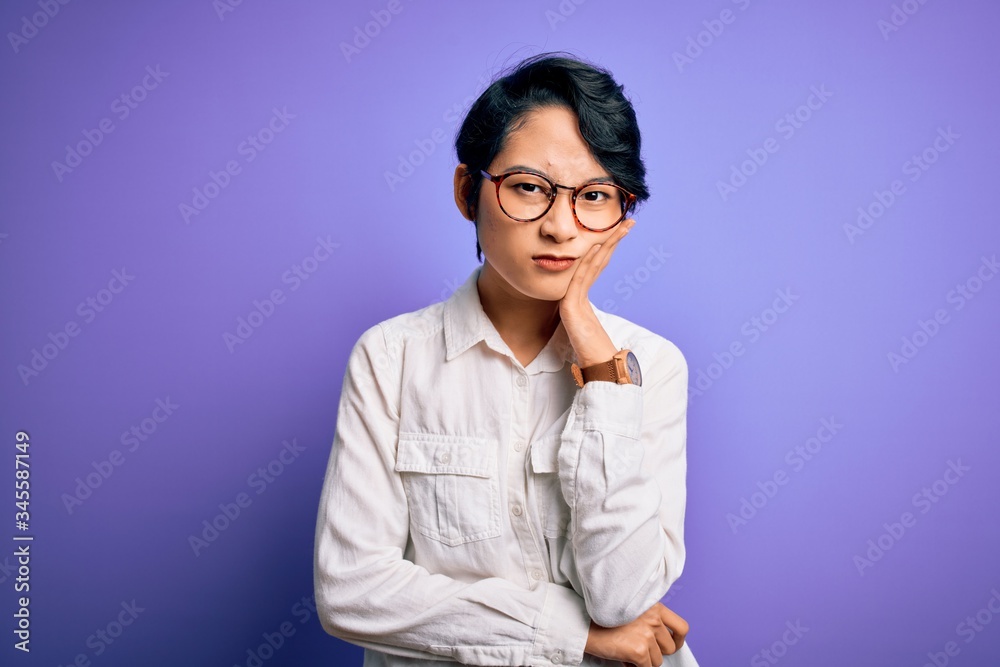 Young beautiful asian girl wearing casual shirt and glasses standing over purple background thinking looking tired and bored with depression problems with crossed arms. Young beautiful asian girl wearing casual shirt and glasses standing over purple background thinking looking tired and bored with depression problems with crossed arms.