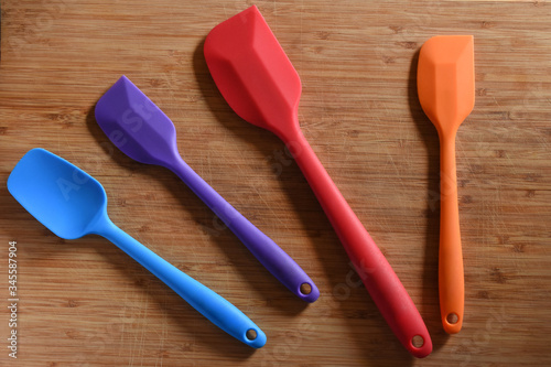 silicone kitchen spatula set, four brightly colored spatulas in two different sizes. Top down view, on a bamboo cutting board.