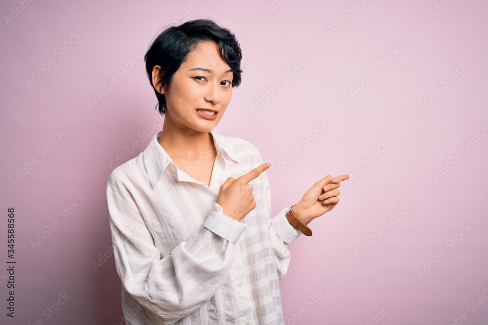 Young beautiful asian girl wearing casual shirt standing over isolated pink background Pointing aside worried and nervous with both hands, concerned and surprised expression Young beautiful asian girl wearing casual shirt standing over isolated pink background Pointing aside worried and nervous with both hands, concerned and surprised expression